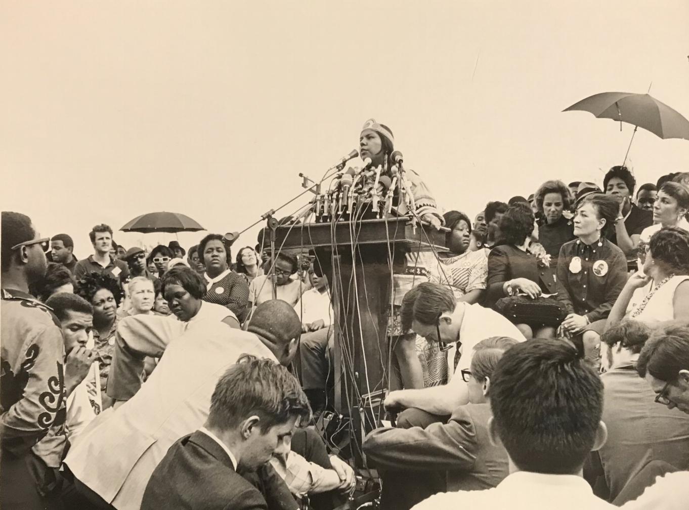 An unidentified speaker takes the podium at the Mother’s Day March organized by Etta Horn and other members of the NWRO. Horn is to the left of the podium in a bright collar and polka dot dress.