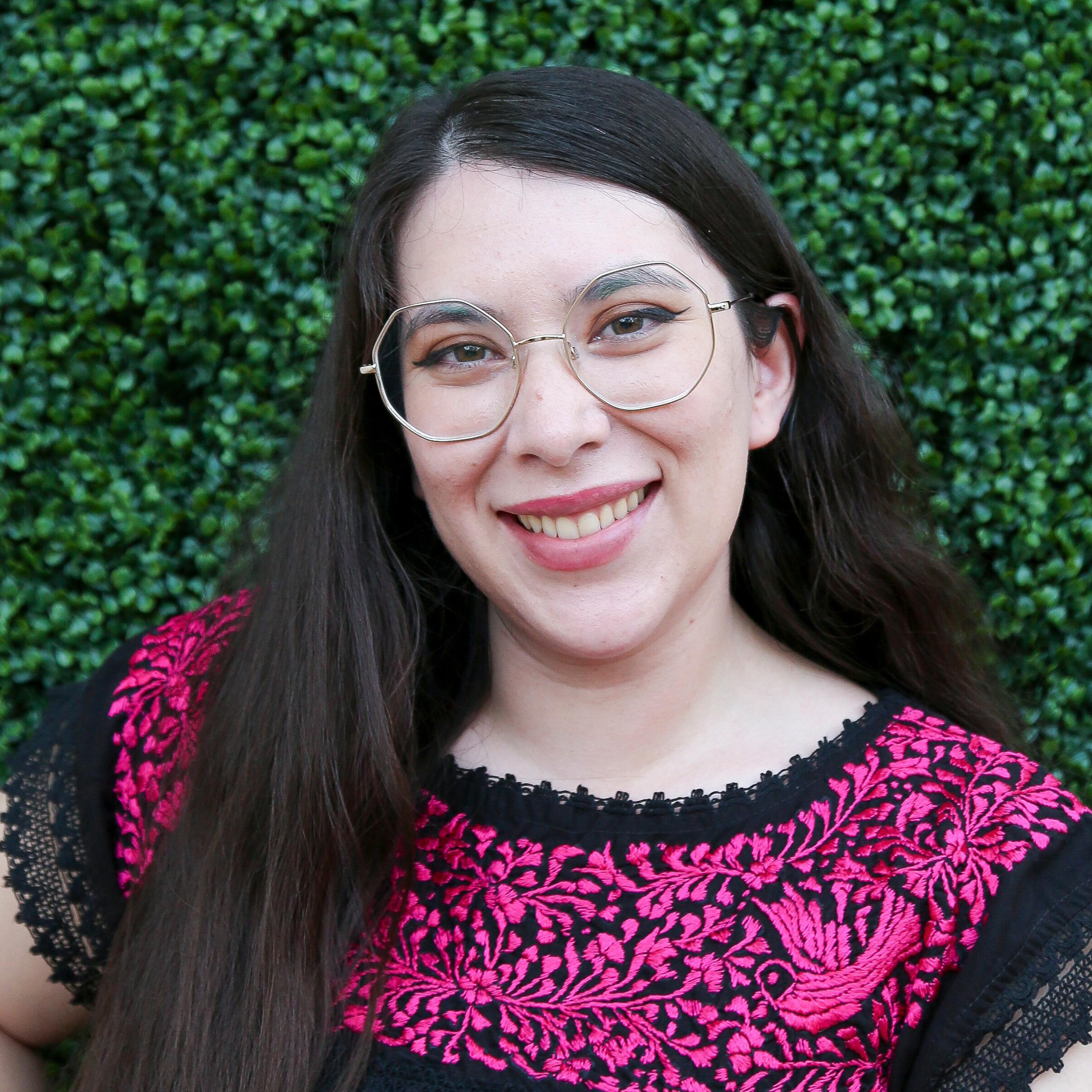 Asami Robledo-Allen Yamamoto standing in front of a green foliage background, smiling.